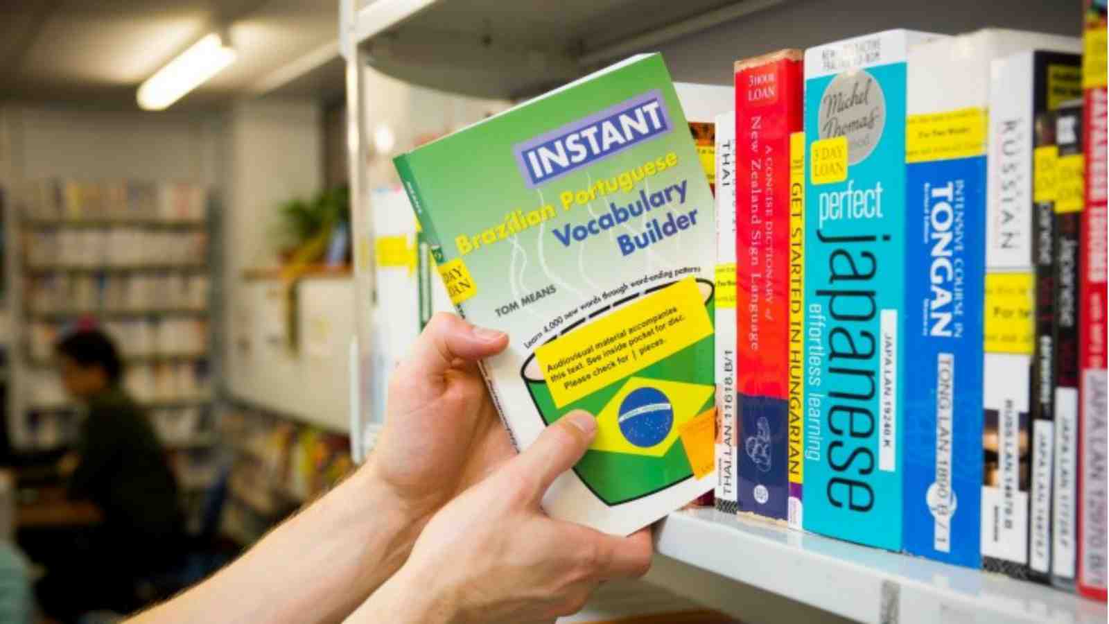 A hand pulls a book off of a bookshelf titled – Instant Brazilian Portuguese Vocabulary builder.