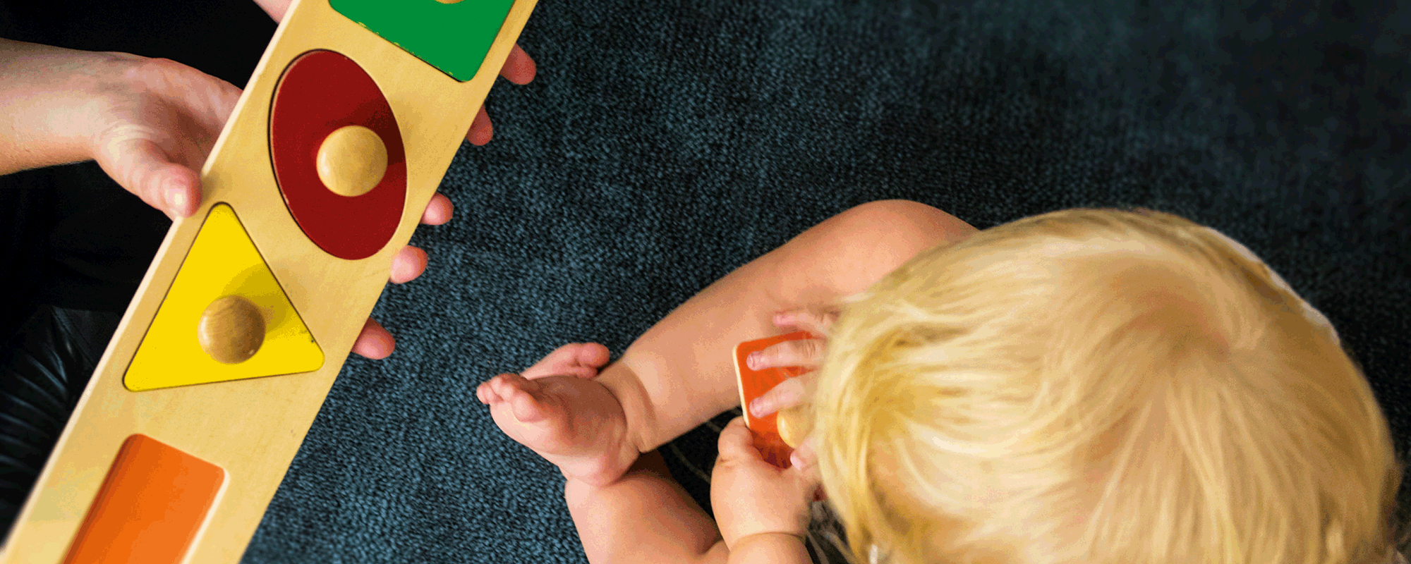 A child playes with wooden shapes the fit into another piece of wood – they are colourful and most of them are in their proper place.