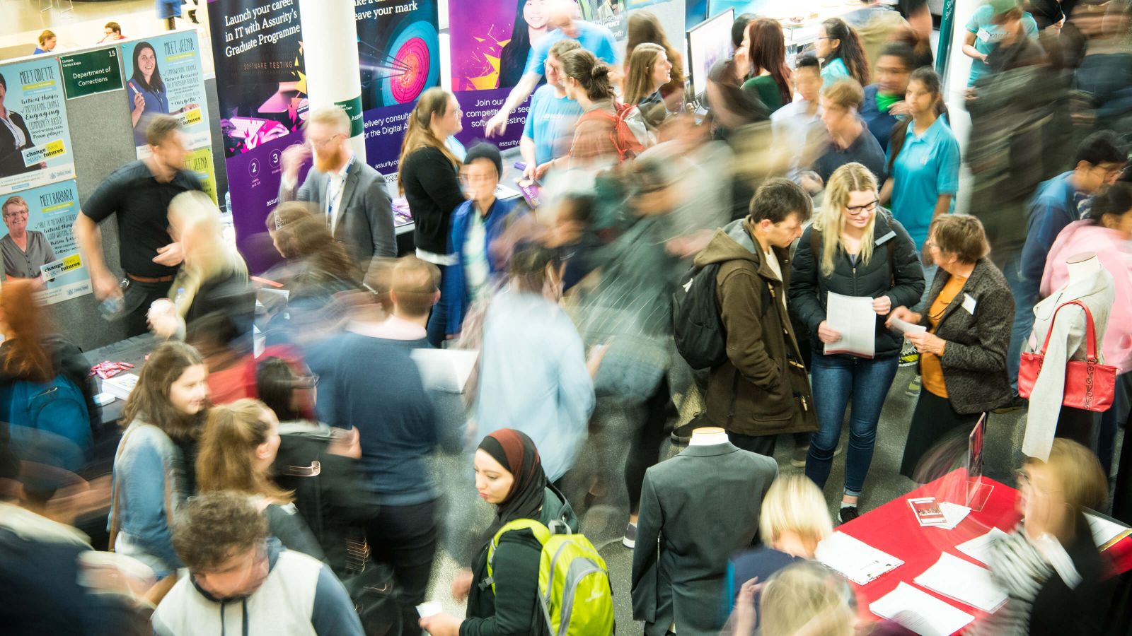 Blurred top-down photograph of students at a crowded careers expo with tables and banners