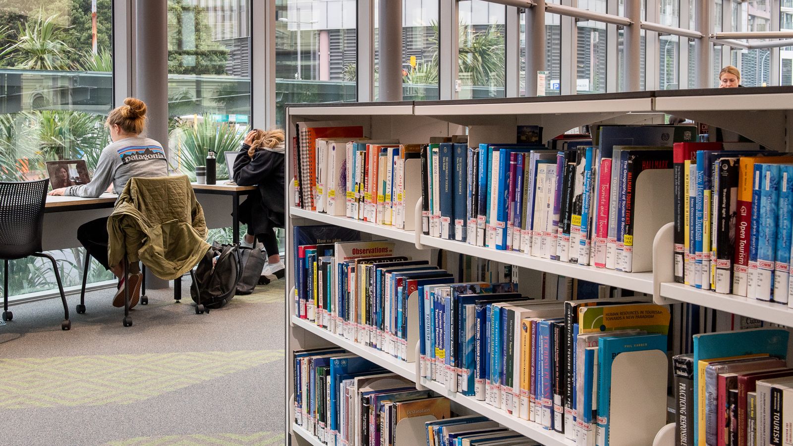 Interior of Pipitea library with bookshelves and some students in the background.