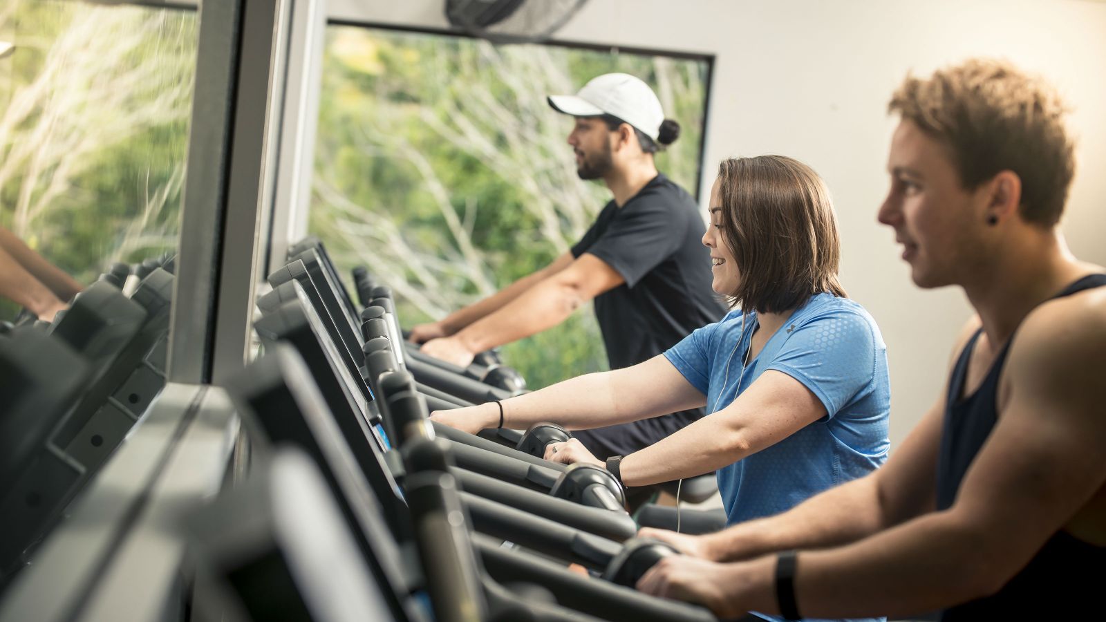 Two men and a woman working out on exercise machines.