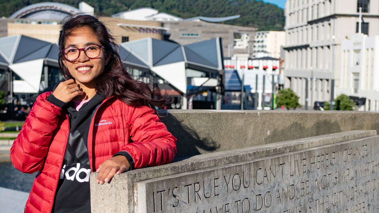 Hla Mynt Thu stands by a wall with downtown Wellington in the background.