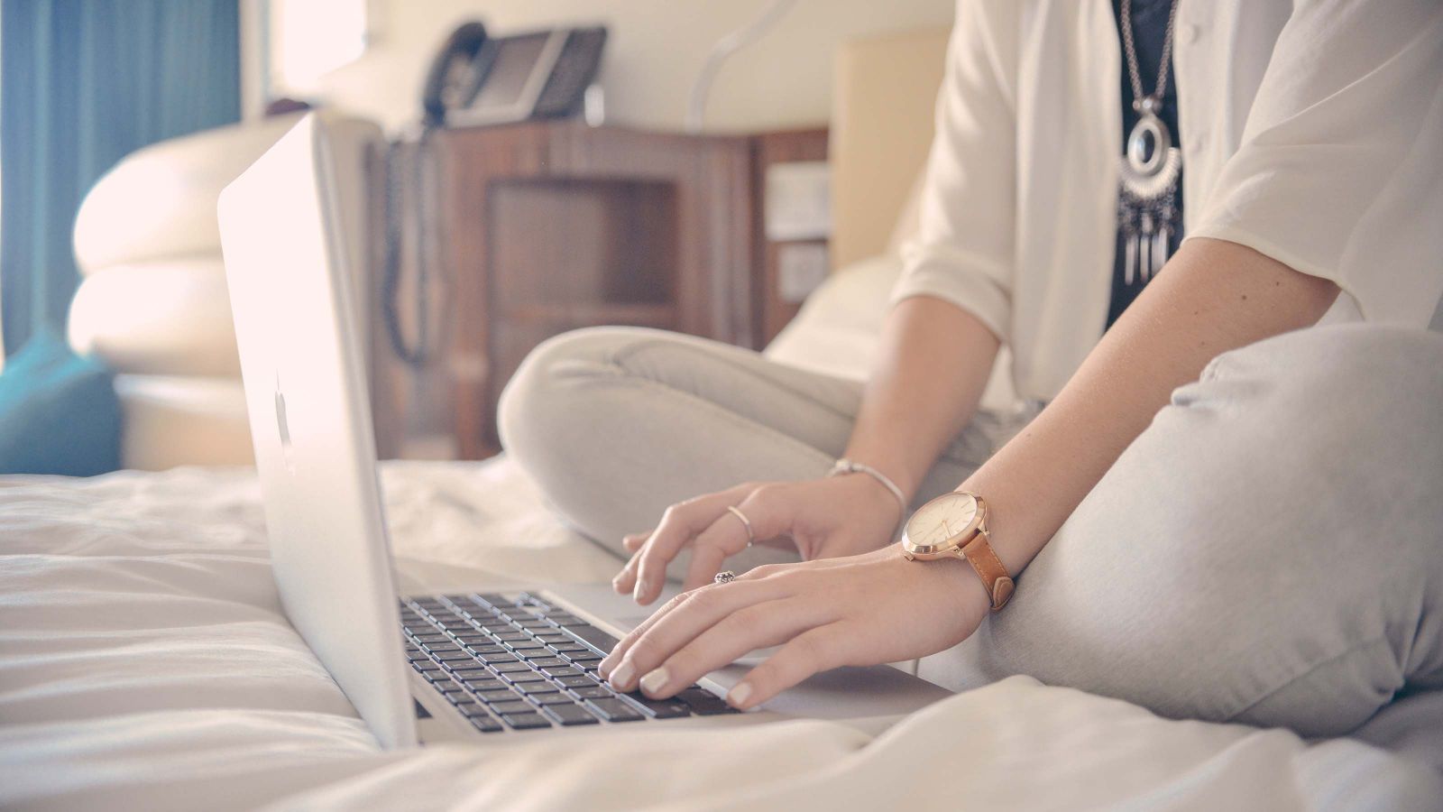 A woman uses an Apple laptop on a bed.