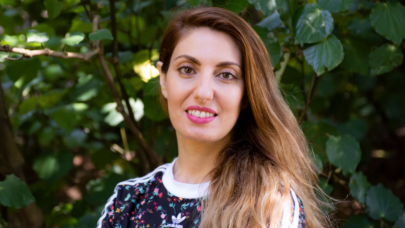 PhD Candidate Joanna Mete posing for a photo in front of green foliage