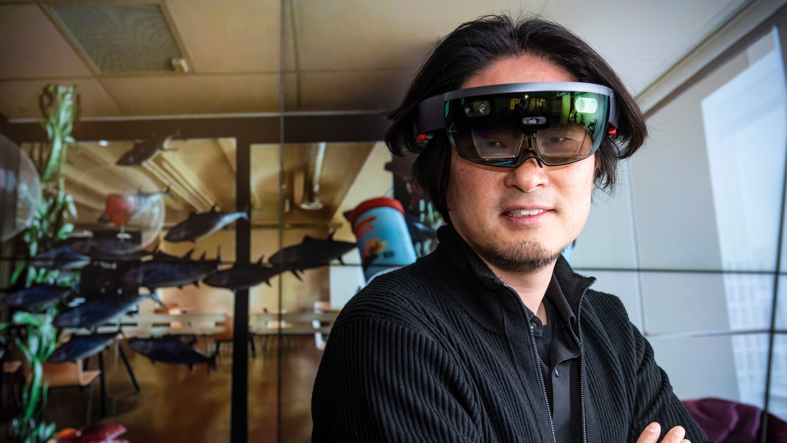 Associate Professor Taehyun Rhee stands in a room wearing a virtual reality headset. Animated fish are floating through the air around him. 