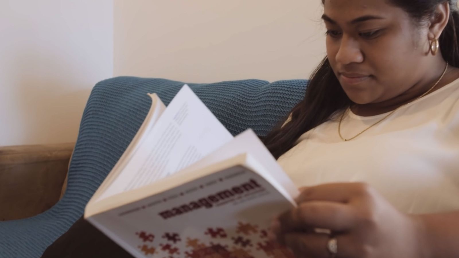 A female student reads a management text book while sitting on a blue couch.