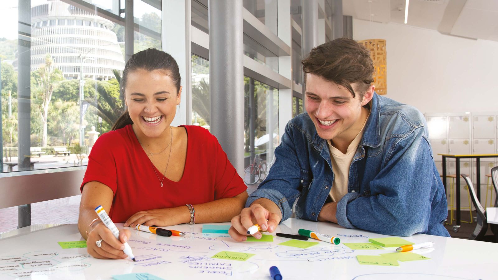 Two students sitting together and writing on a white board in a seminar room at the university’s Pipitea campus.