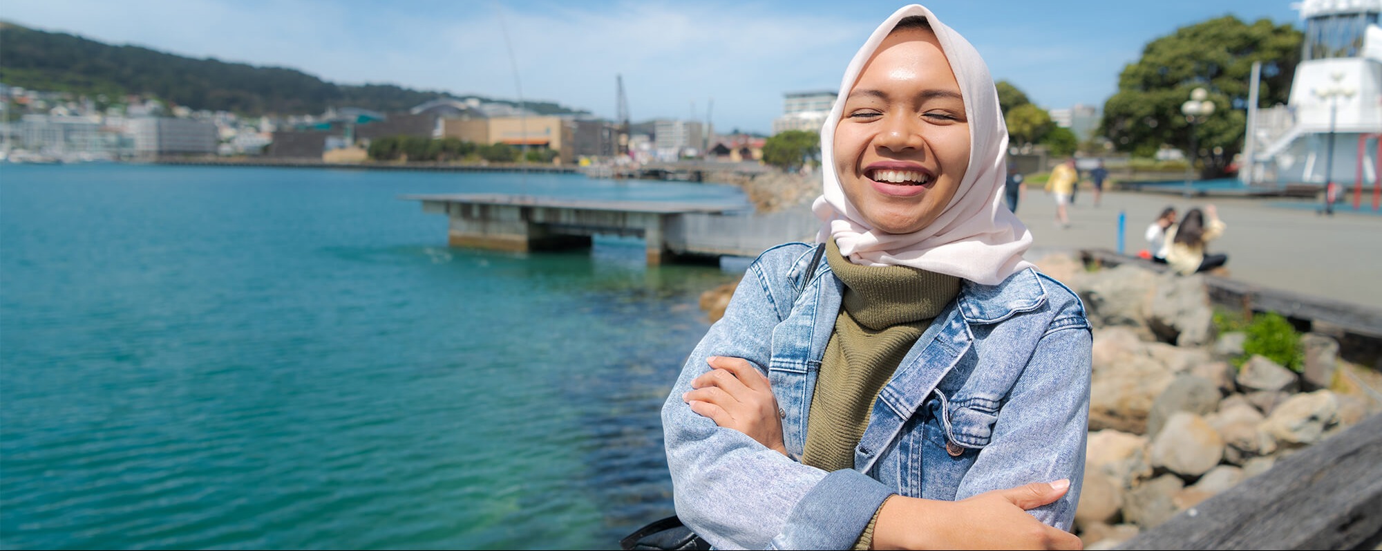 International student Tasha Waris standing by waterfront and laughing confidently.