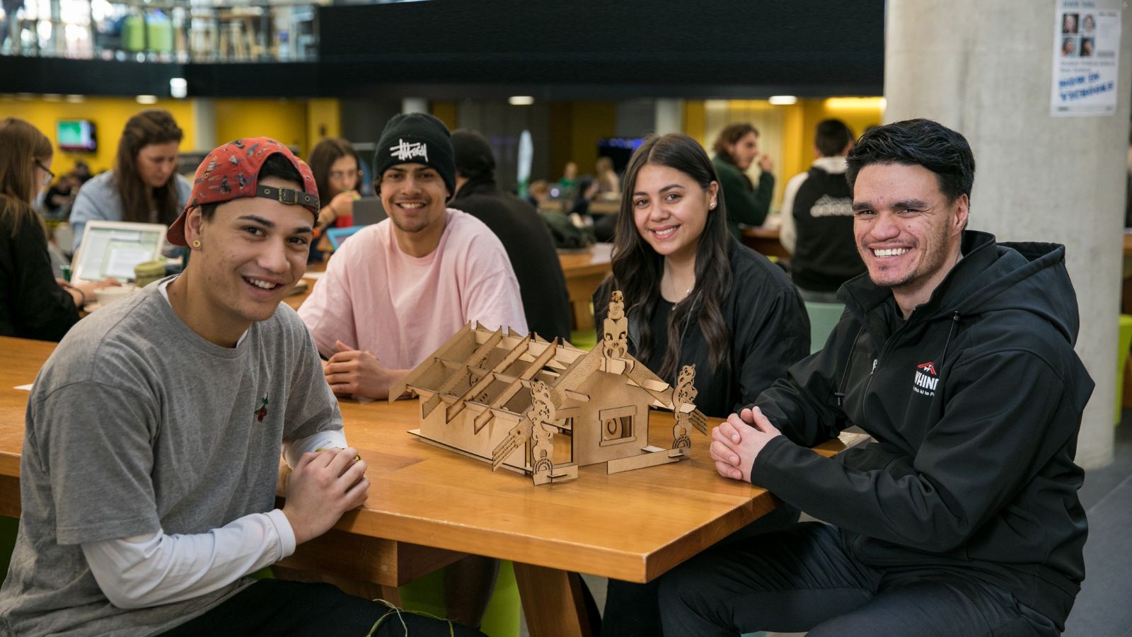 3 boys and 1 girl sitting at a table in the Hub, with a wooden model of a marae on the table in the middle of them.