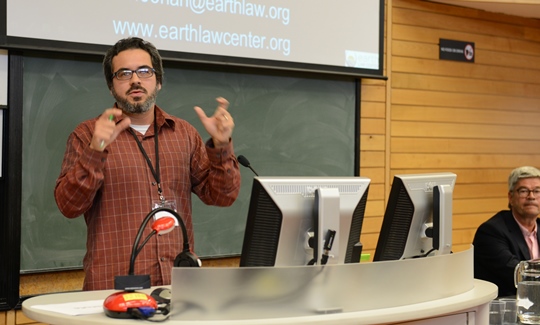 A professional man stands at the front of a lecture hall giving a presentation.