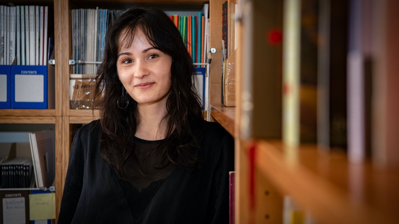 Millie Riddell leaning against shelves in the New Zealand Art Archive administered by Adam Art Gallery