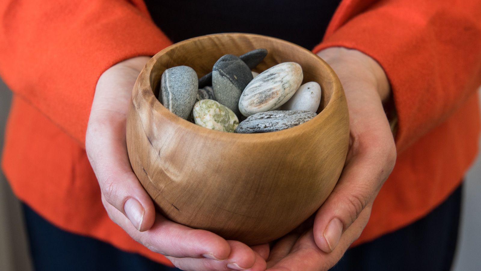 Two hands holding a wooden bowl with rocks inside.