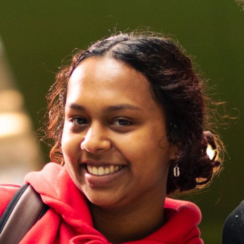 A head and shoulders portrait of a smiling, female student wearing a red hoodie.