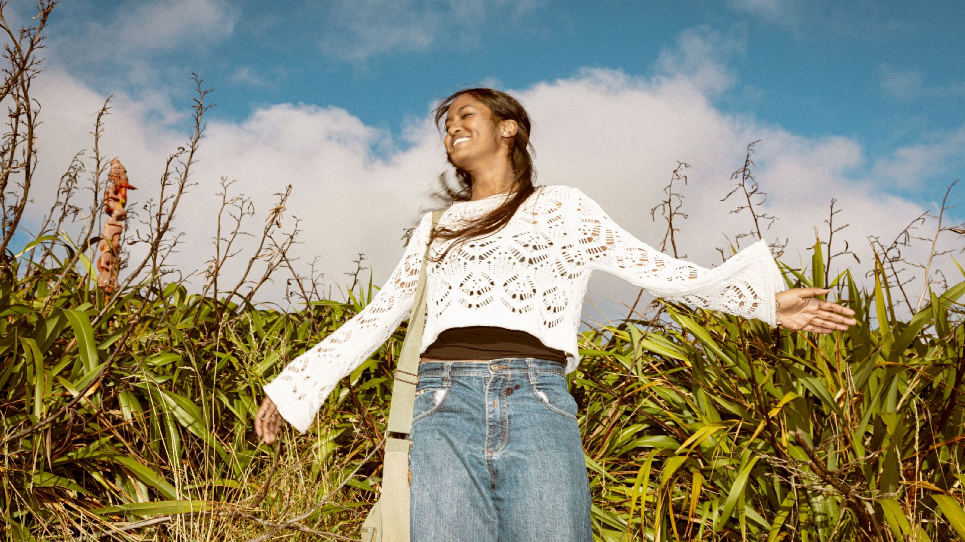Female student is standing outside with her arms outstretched and the sky and grass are around her