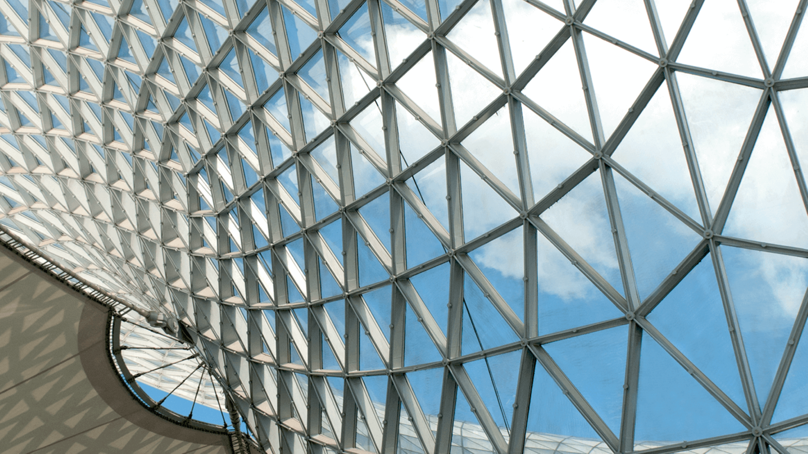 A geometric roof made with glass and many triangles with blue sky in the background.