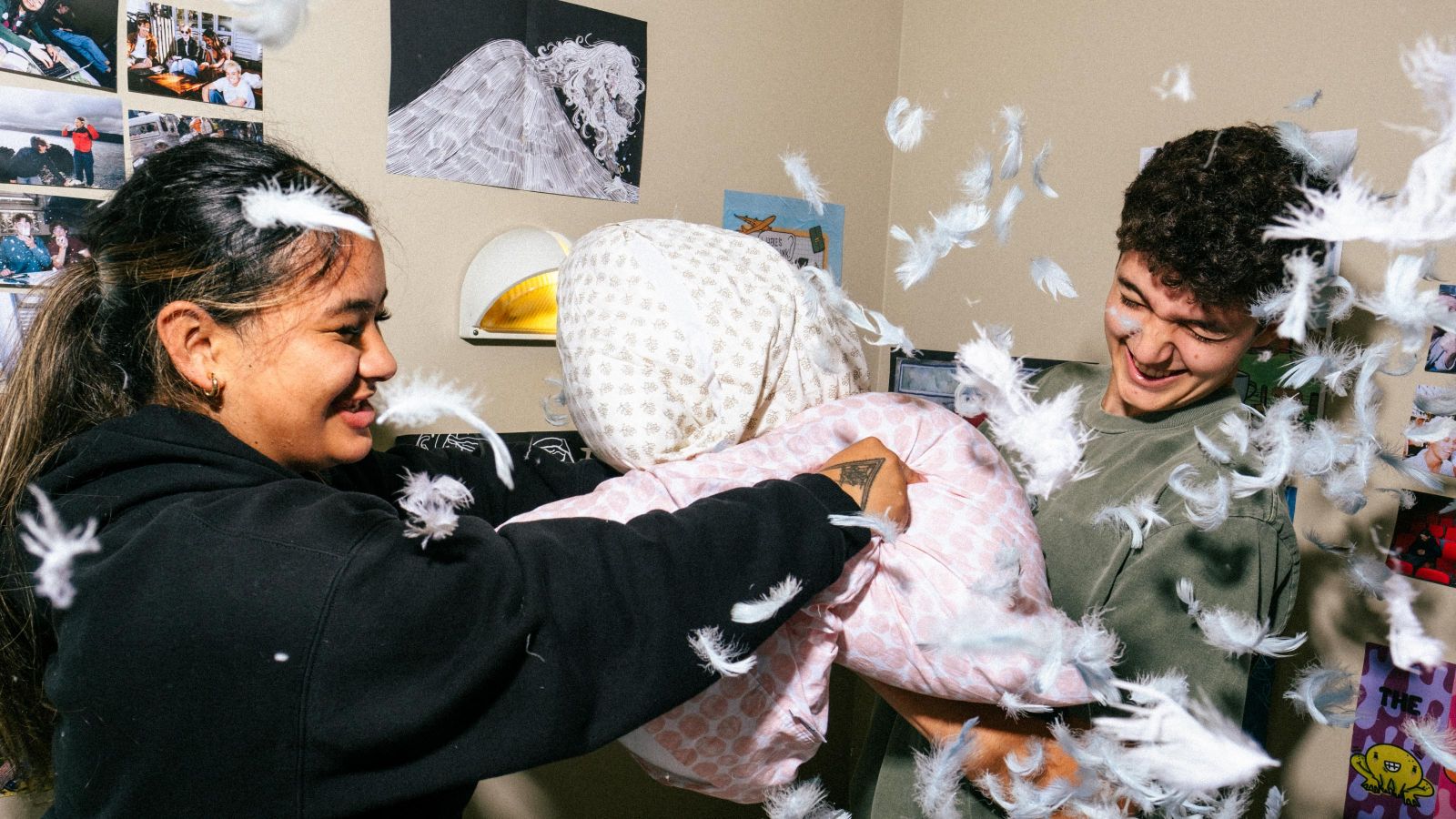 two students in a halls of residence having a pillow fight with feathers falling out