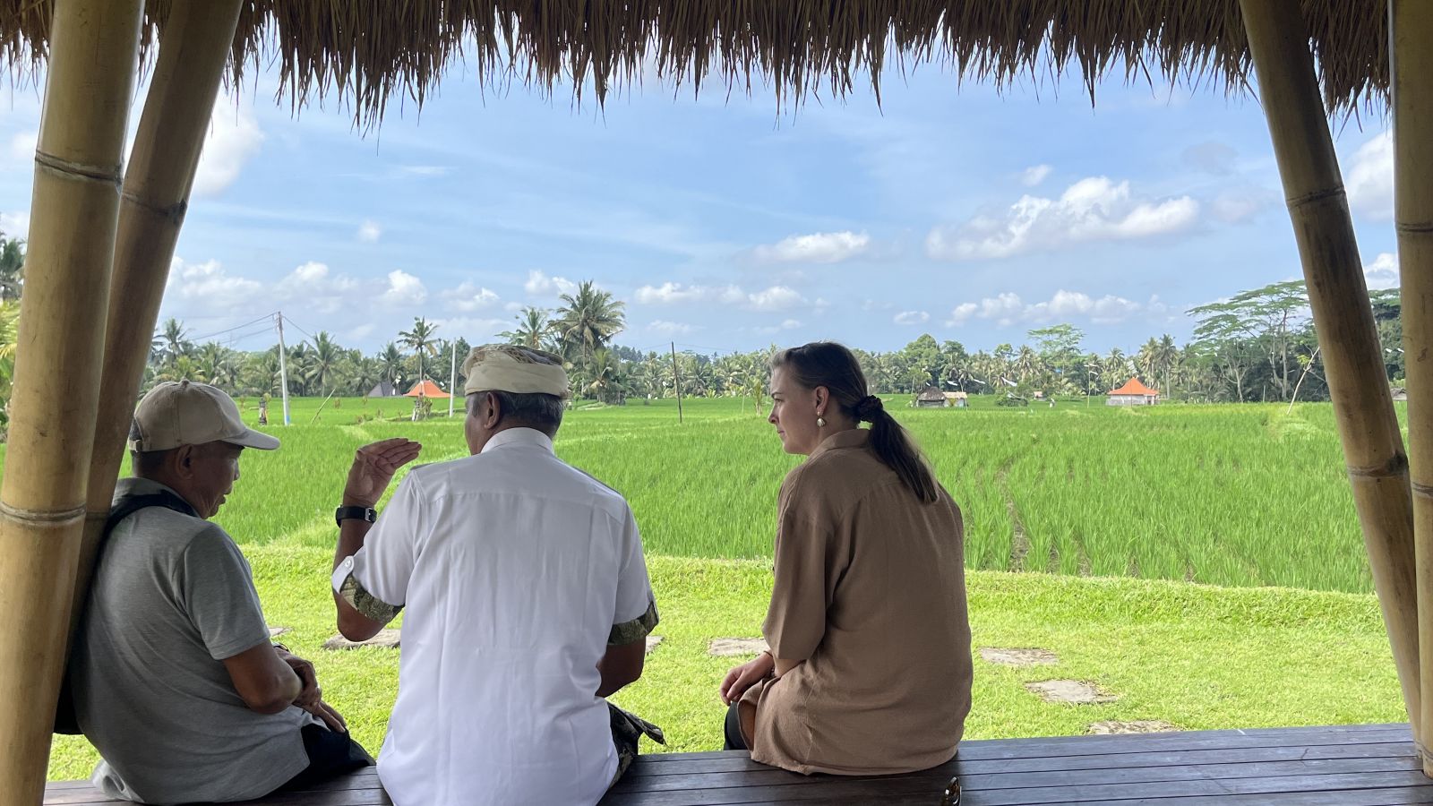 Annabel is sitting with two local people in a Bali landscape