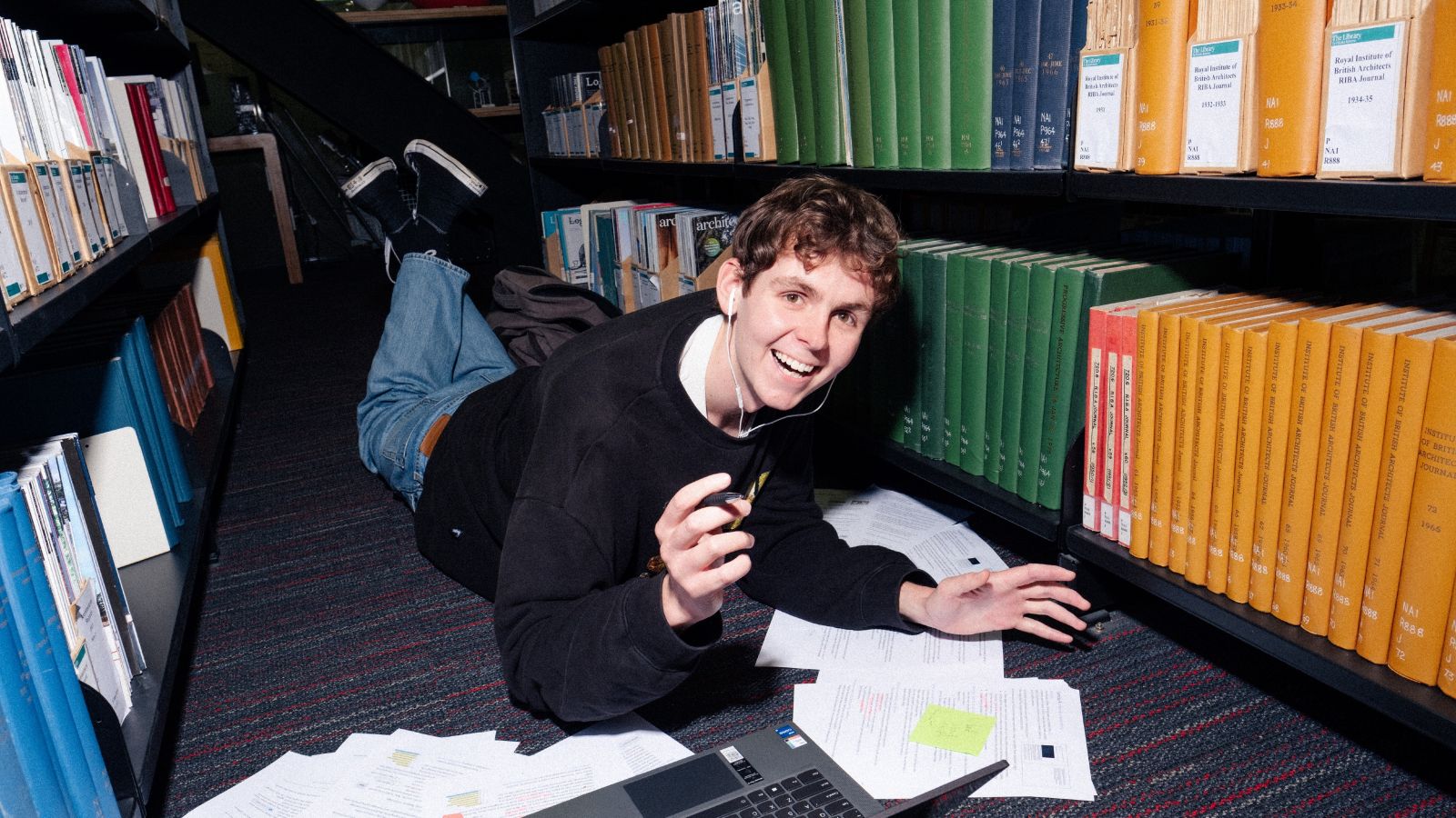 Student studying by himself on the ground in the library surrounded by notes