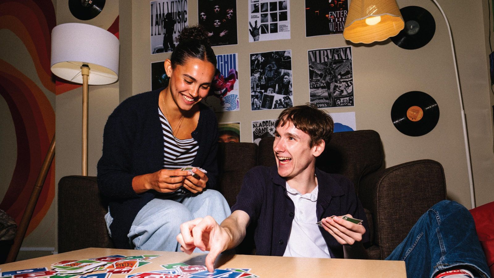 Two students sitting on the couch in student accommodation playing uno cards.