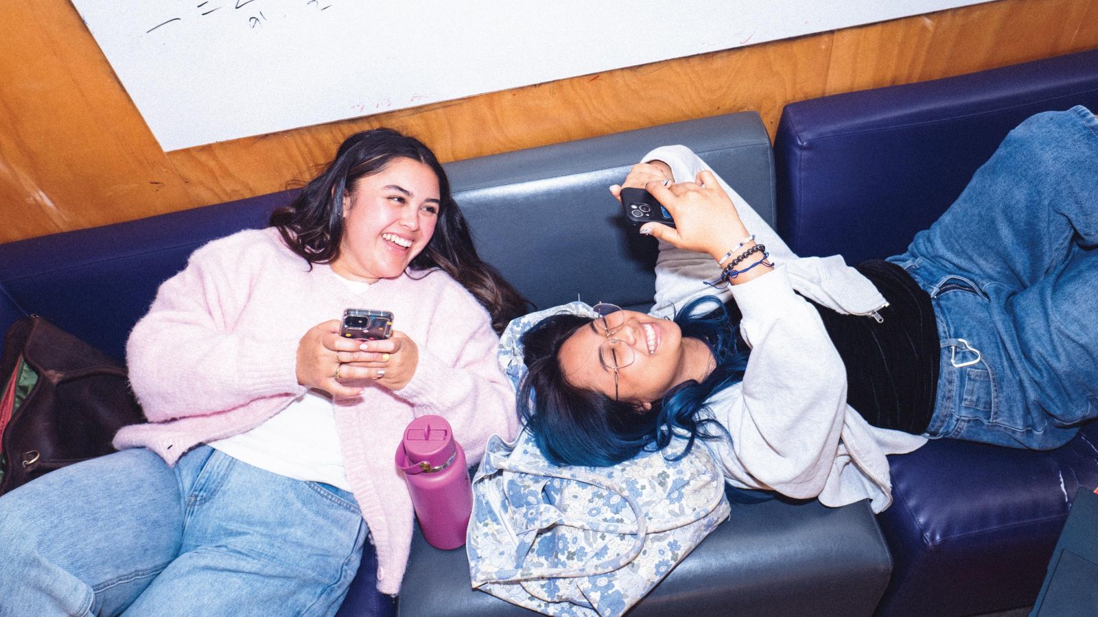 Two female students lying on a couch and laughing together.
