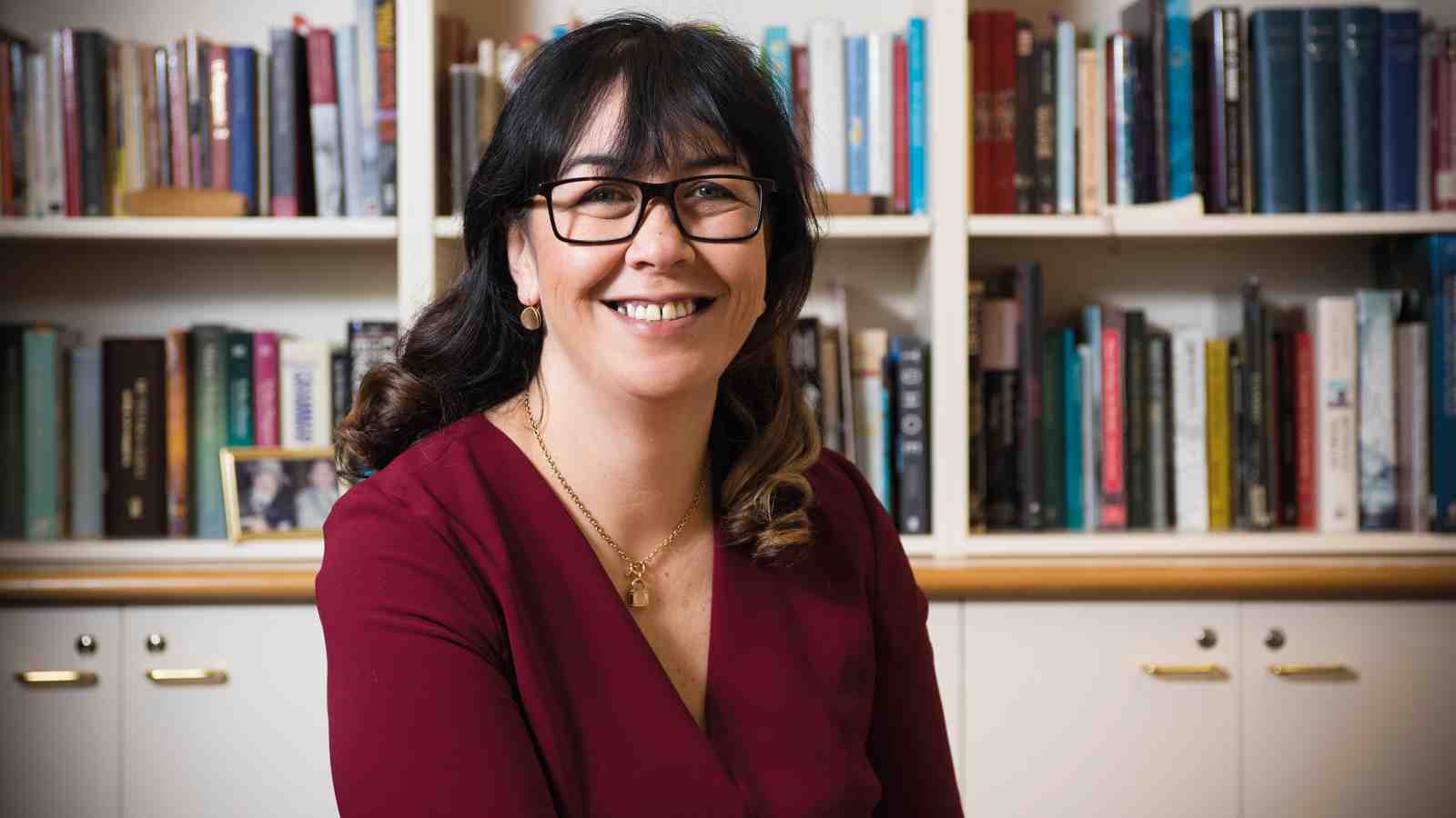 Professor Rawinia Higgins sitting in her office in front of her wall of bookshelves.