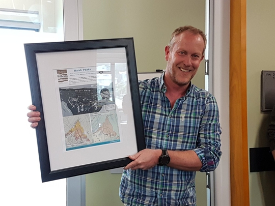 Prof. Tim Naish holding a framed picture of the location of the Naish Peaks, Antarctica