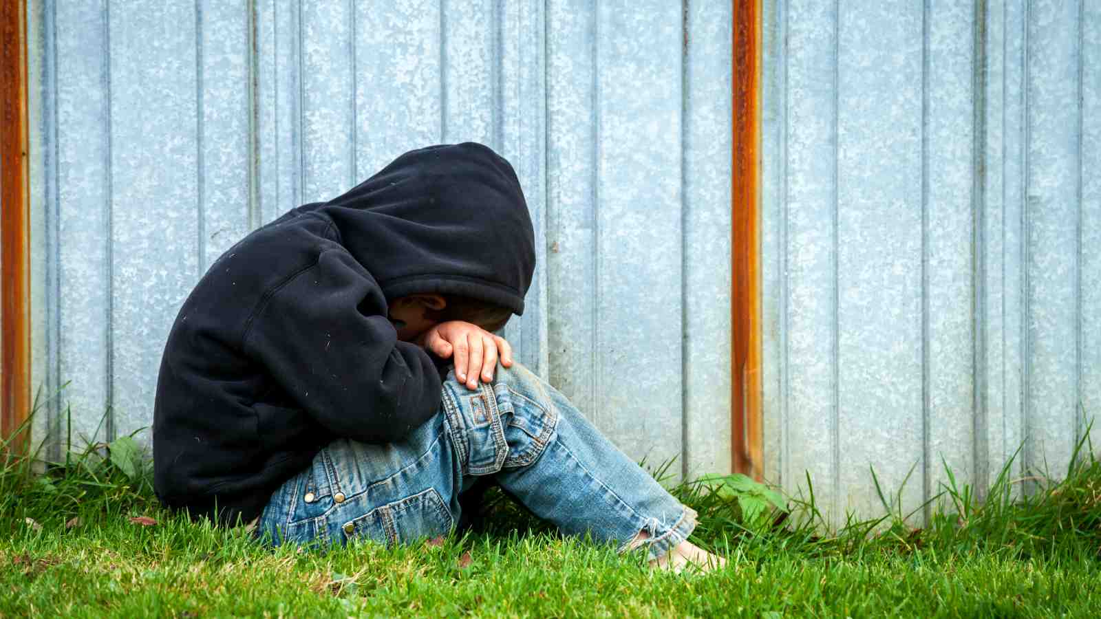 A child shelters beside a fence.