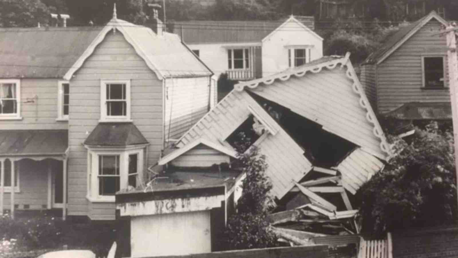 A black and white image of houses in a street, the house on the right has collapsed.