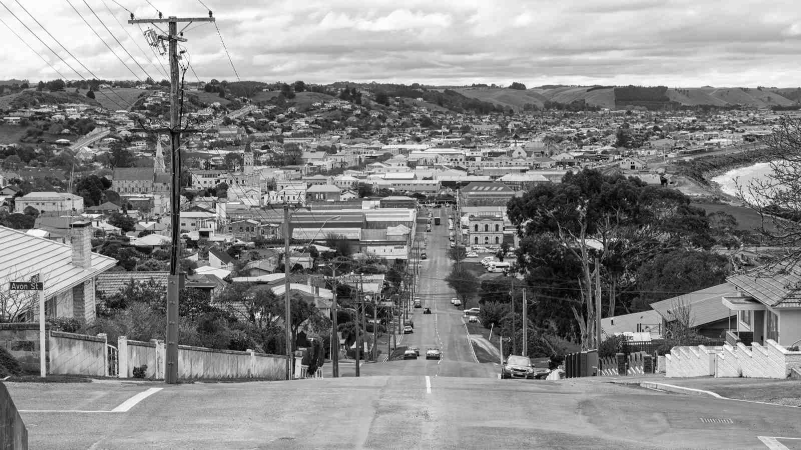 A long road pictured in black and white, that slopes down towards a city.