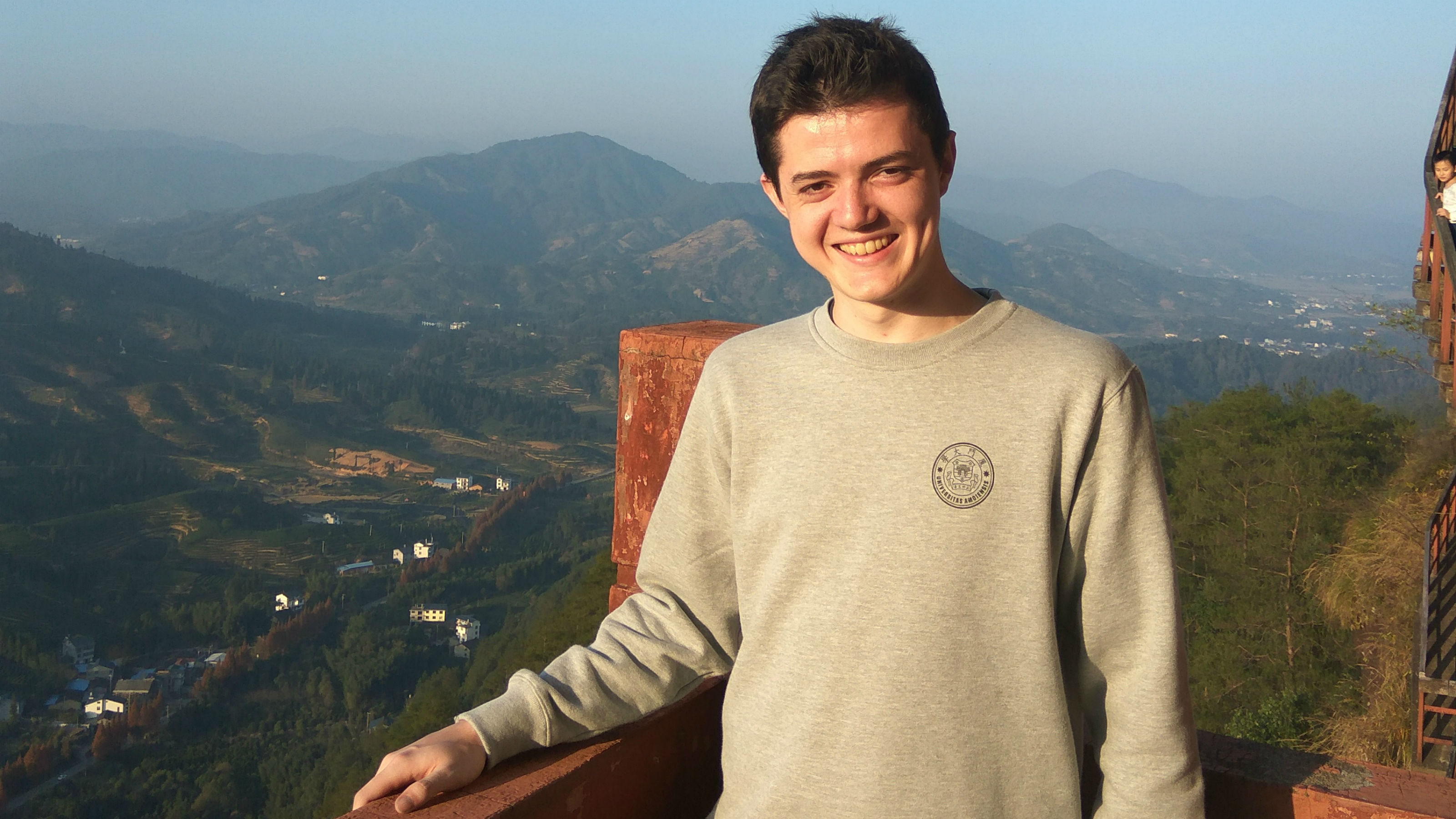 Ed on exchange in China, standing in front of a hilly landscape.