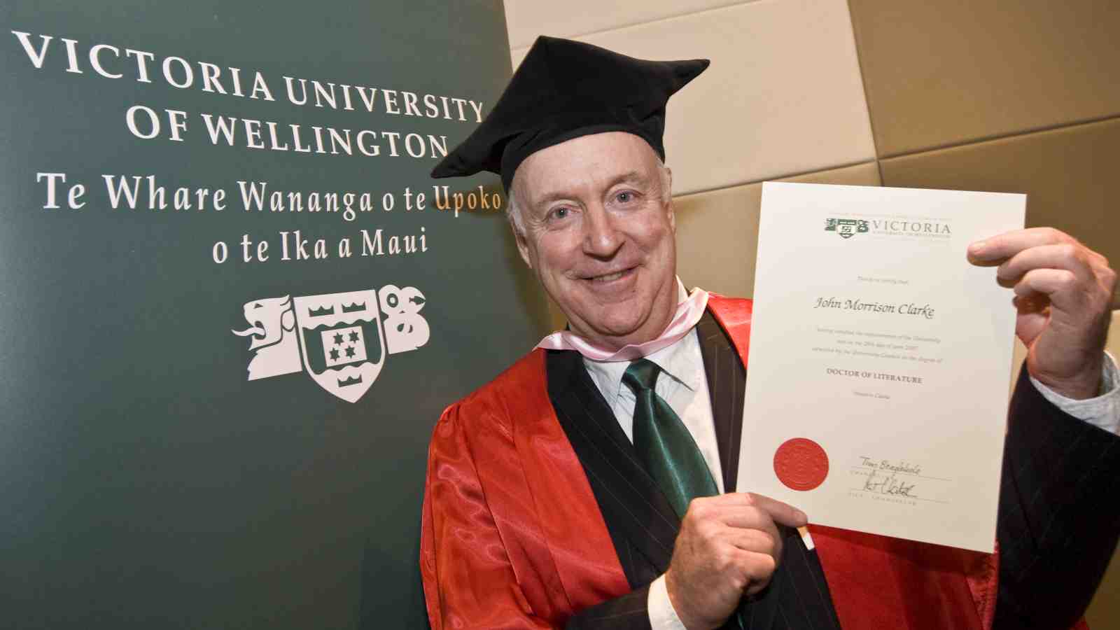 John Clarke holds up his Doctor of Literature.