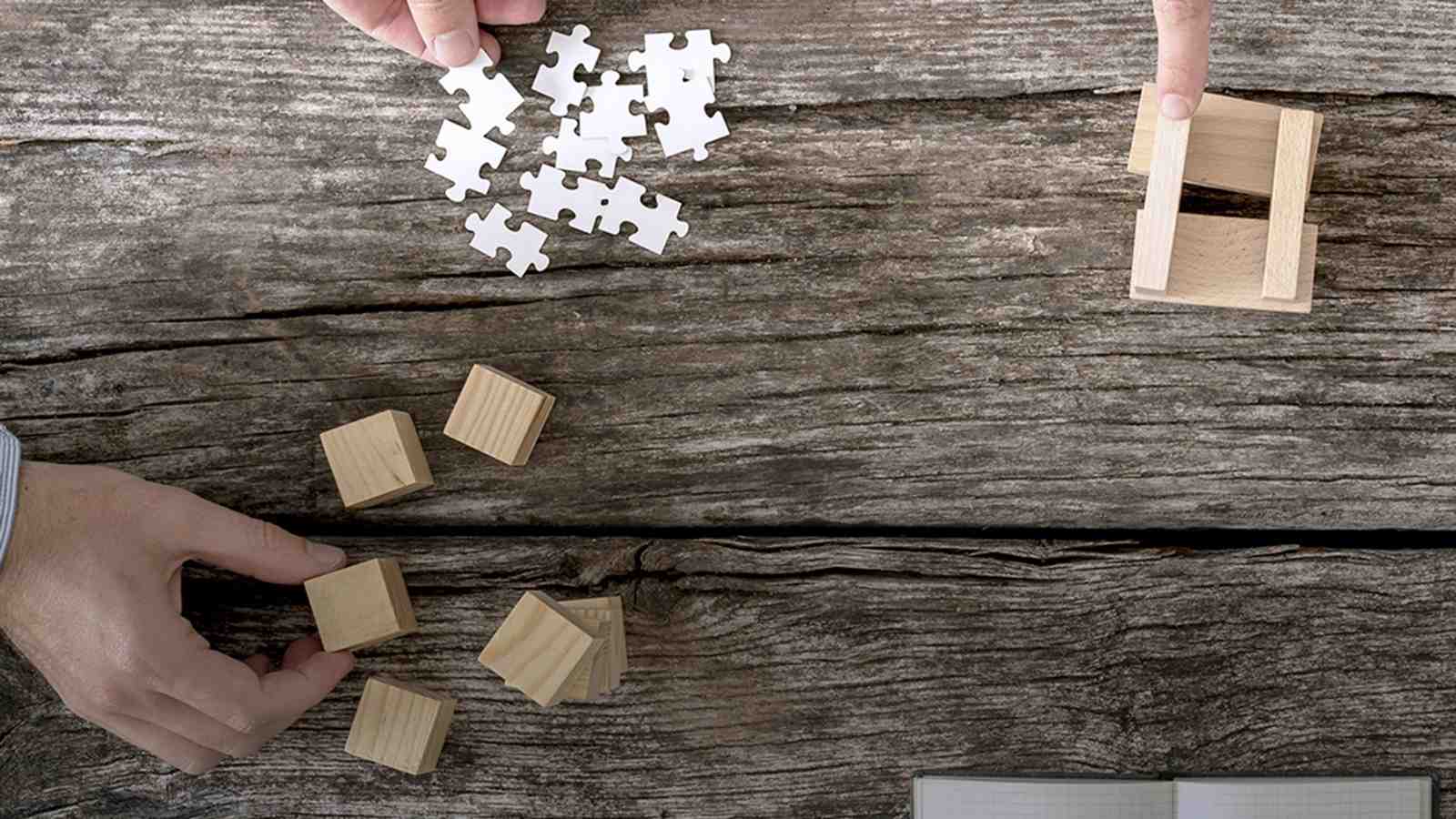 An overview of a wooden table with hands moving small cubes, puzzle pieces and small pieces of wood.