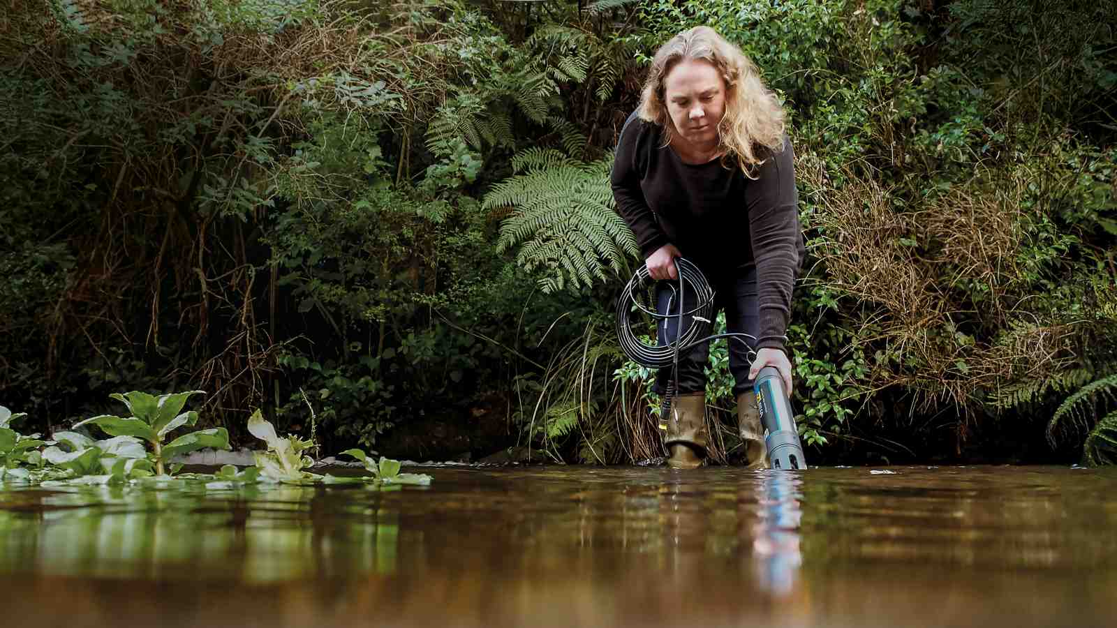 Researcher Bethanna Jackson tests her newly developed tool LUCI that can help farmers manage nutrient loss in waterways. She is standing in a river and the tool is in the water. 