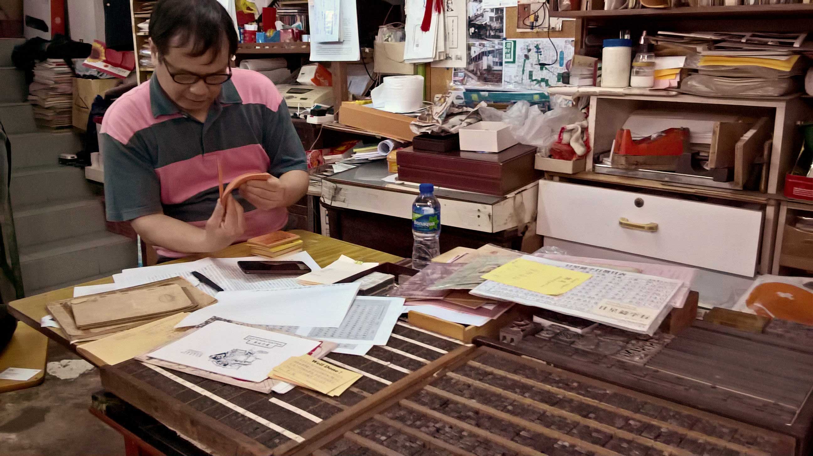 Master printer Yam Wai-Sing (Sam) of Kwong Wah Printing Company reads notes from past students in his print shop