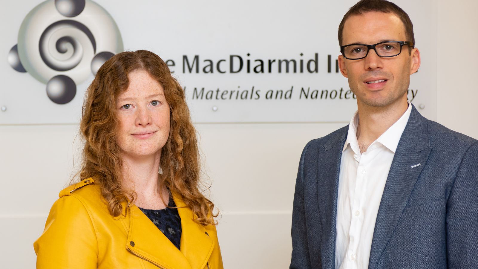 Associate Professor Nicola Gaston and Associate Professor Justin Hodgkiss stand in front of the MacDiarmid Institute name and logo.