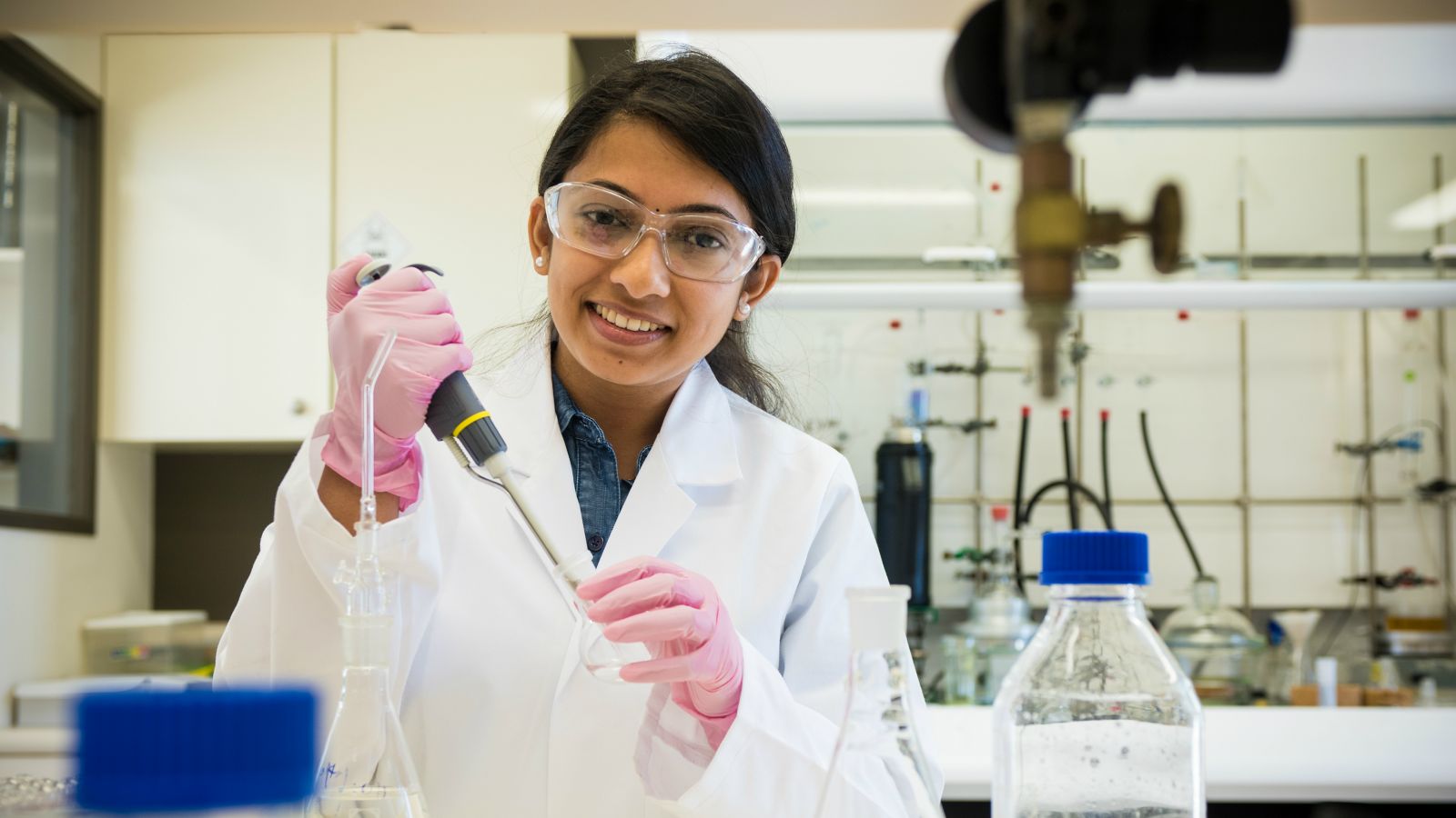 Photograph of Juby Mathew in a laboratory using a pipette and a round based flask.