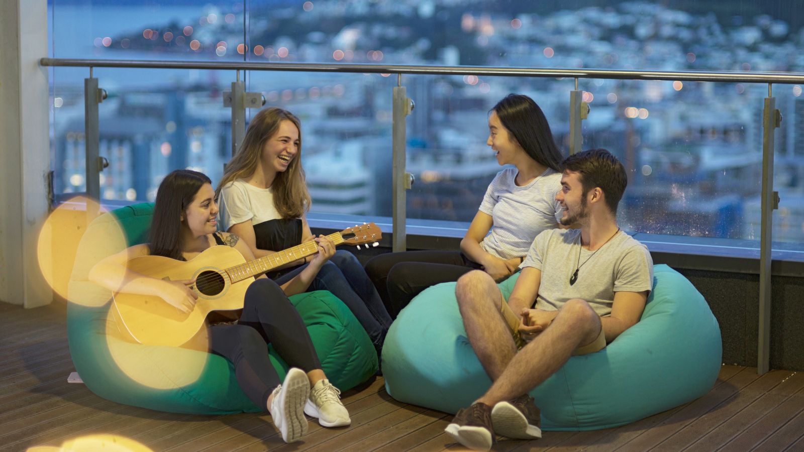 Students sit in beanbag chairs and socialise together – one plays a guitar.