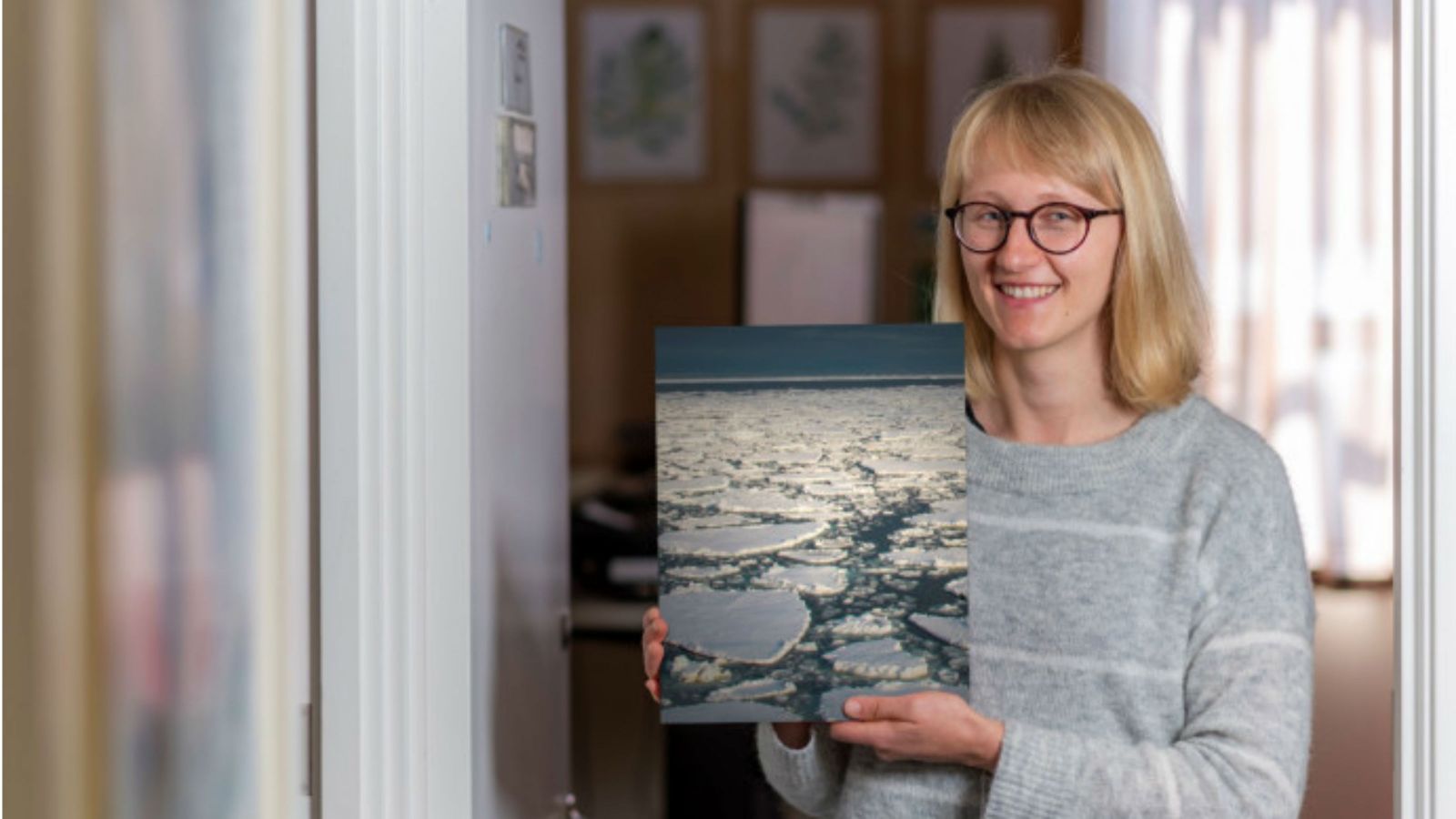 Lettie stands in a hallway holding up an image showing Antarctic ice