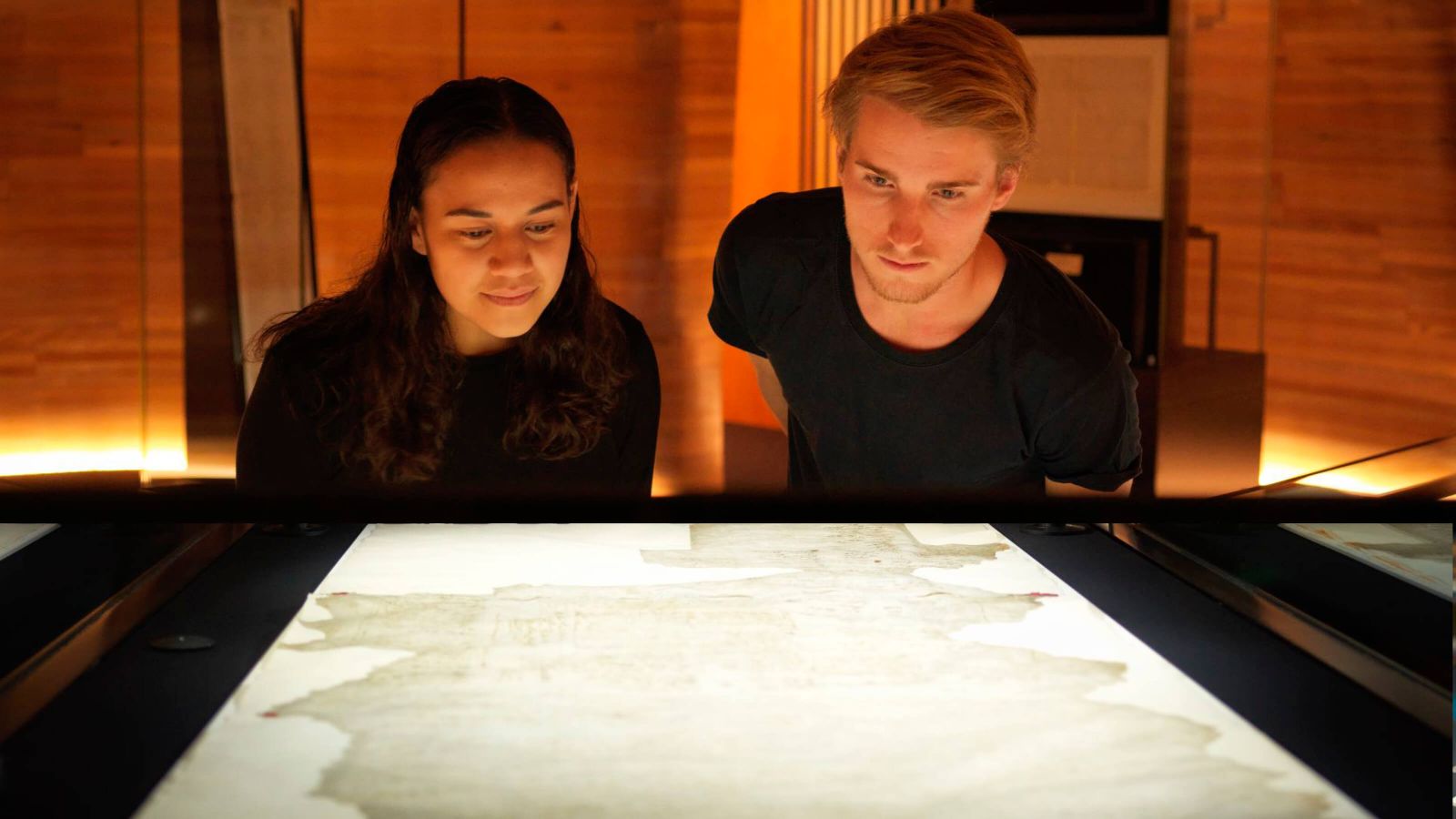Two History students are looking down at the Treaty of Waitangi which is on display at the National Library of New Zealand, Wellington.