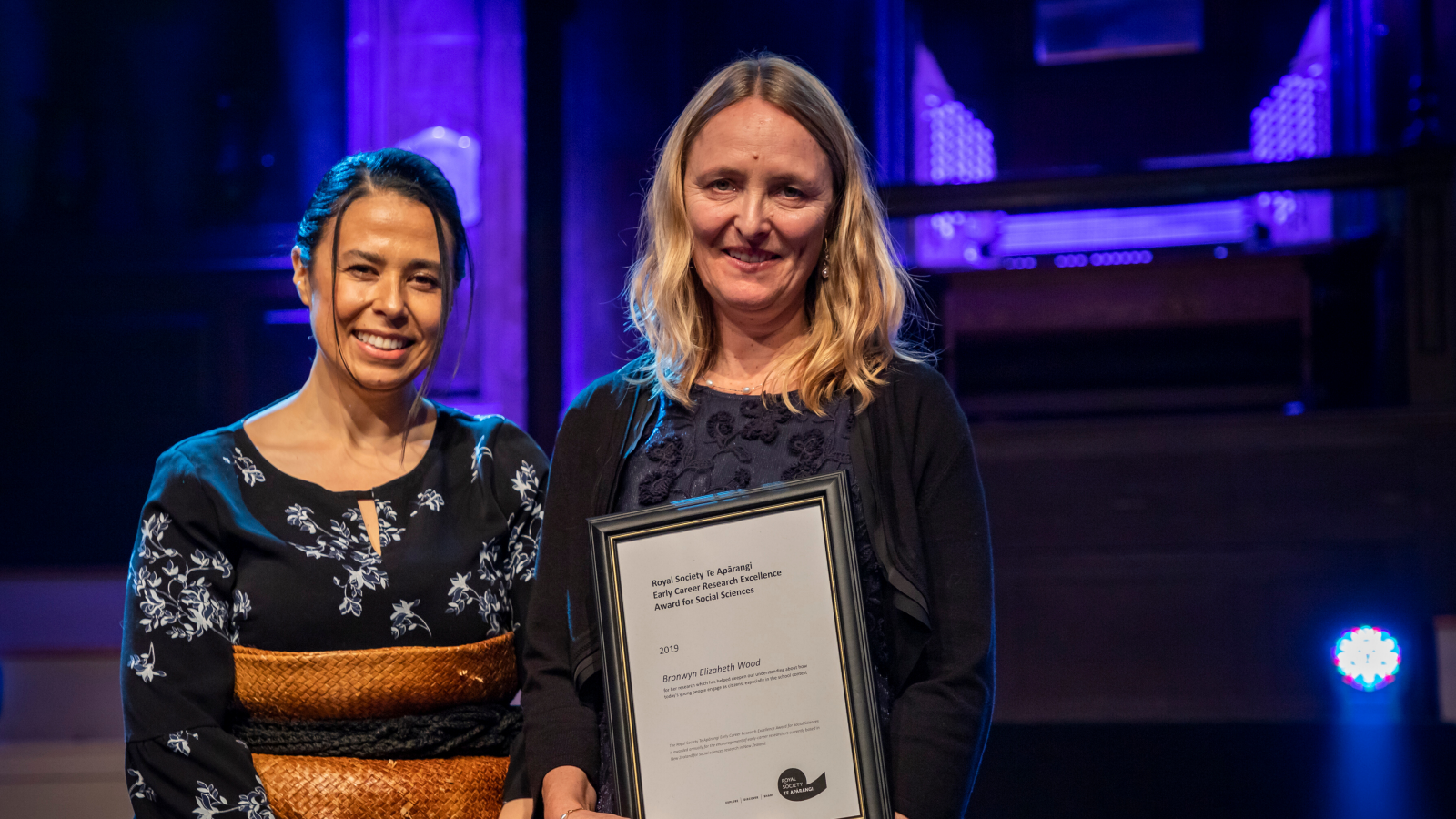 Dr Dianne Sika-Paotonu and Dr Bronwyn Wood stand on a stage holding an award.