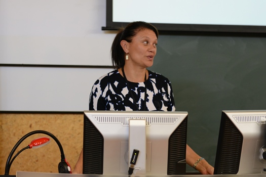 A professional woman gives a presentation at the front of a lecture hall.