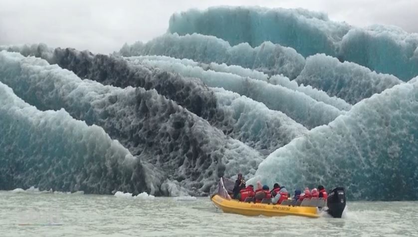 A boat full of people drives closely to interesting glacial ice formations.