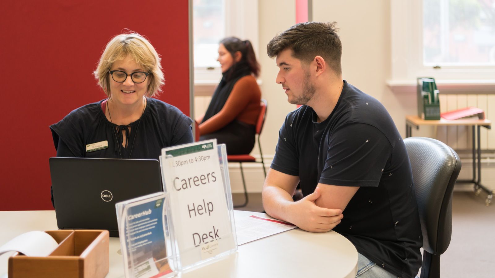 Student sitting at a table with a student career adviser, looking at a laptop screen.