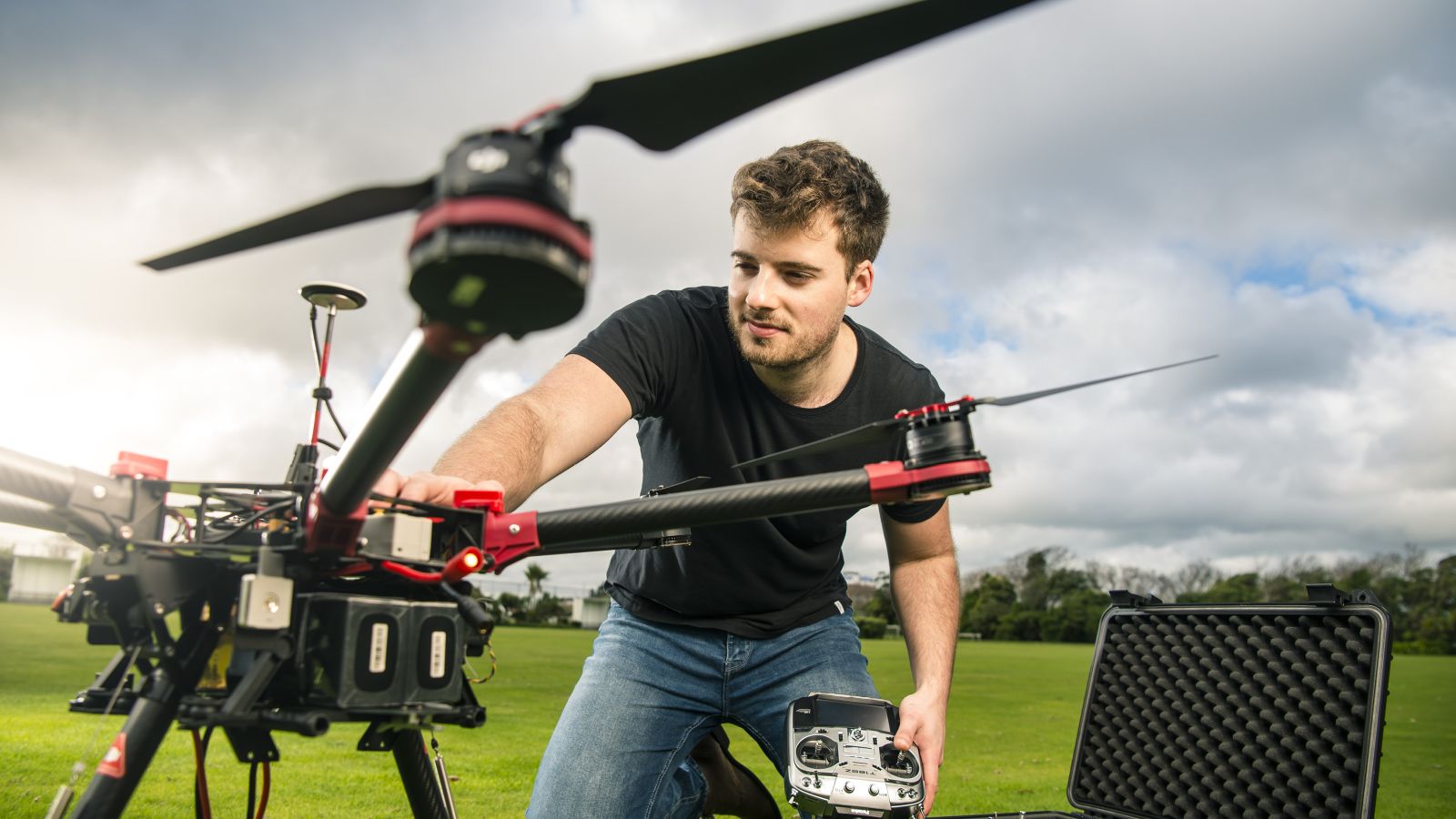 A male student in a field with a large drone, getting it ready to operate.