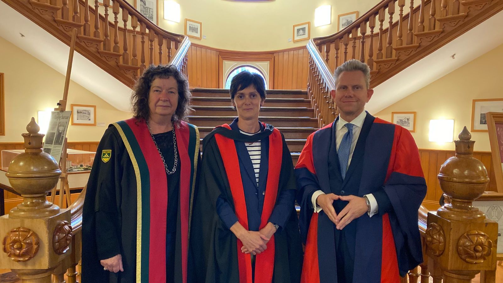 Three academics in formal robes - from left to right Provost Professor Wendy Larmer, Professor of Law Nicole Moreham and Pro Vice-Chancellor Professor Mark Hickford - standing at the foot of an impressive wooden staircase in the Old Government Building.