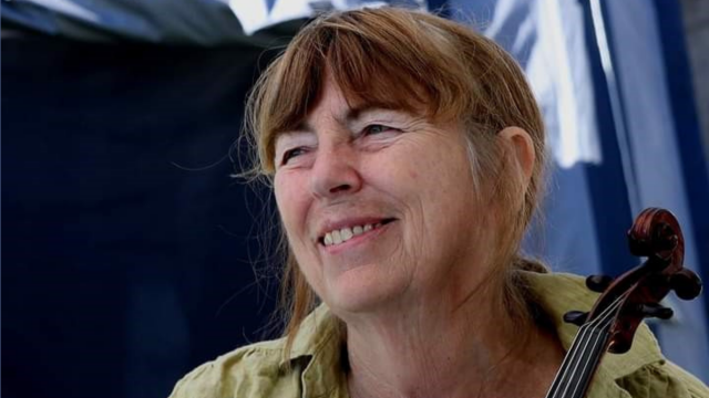 woman with smiling face looking into distance holding top of violin