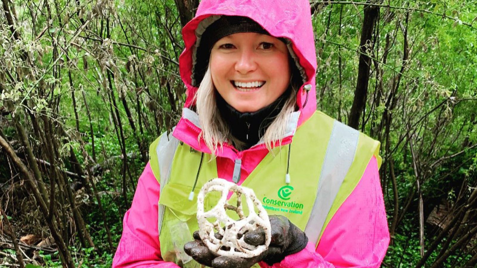 Student in forest holding fungus wearing Conservation Volunteer New Zealand vest.  