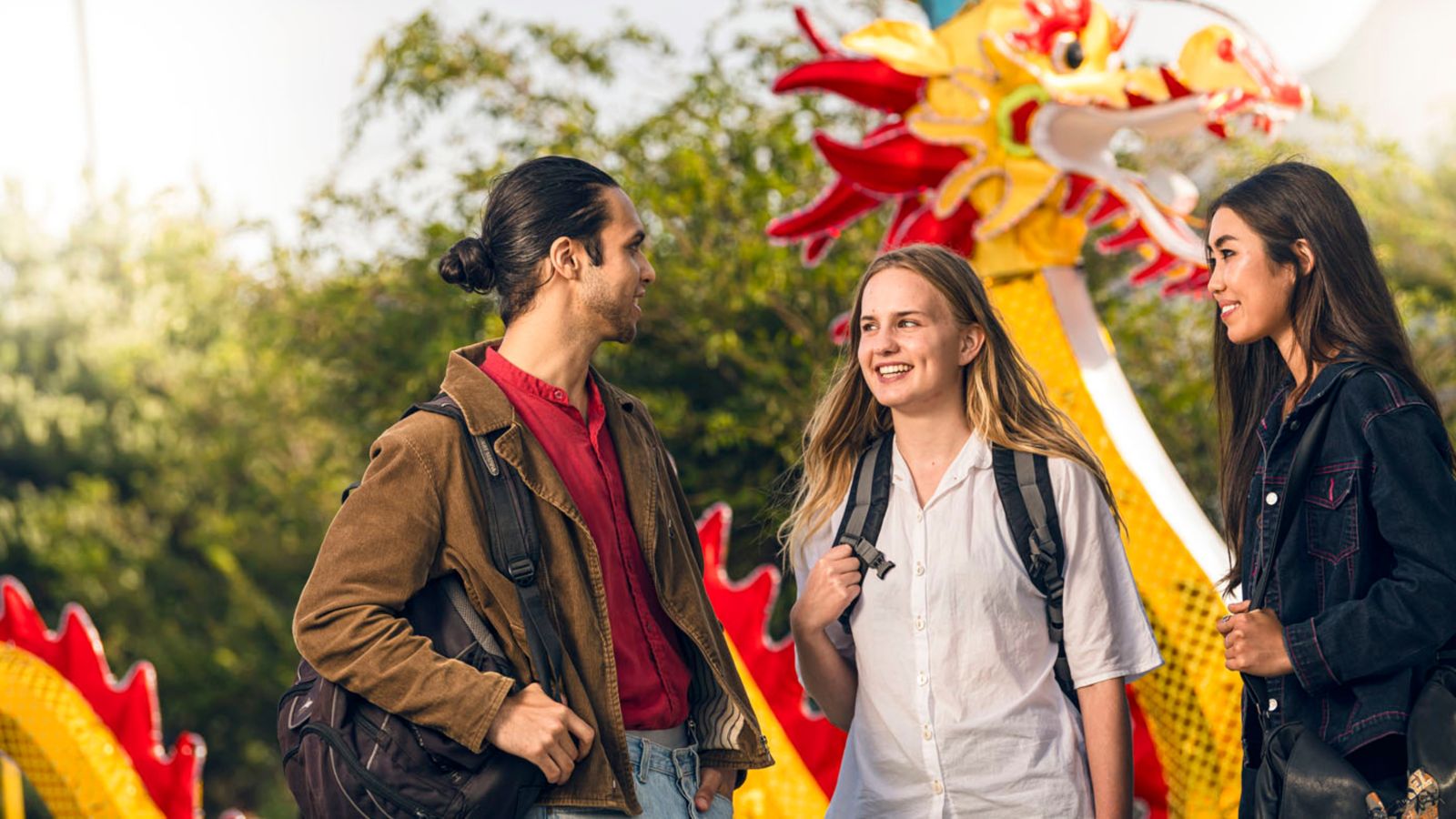 Three students in conversation, standing in front of a Chinese dragon banner