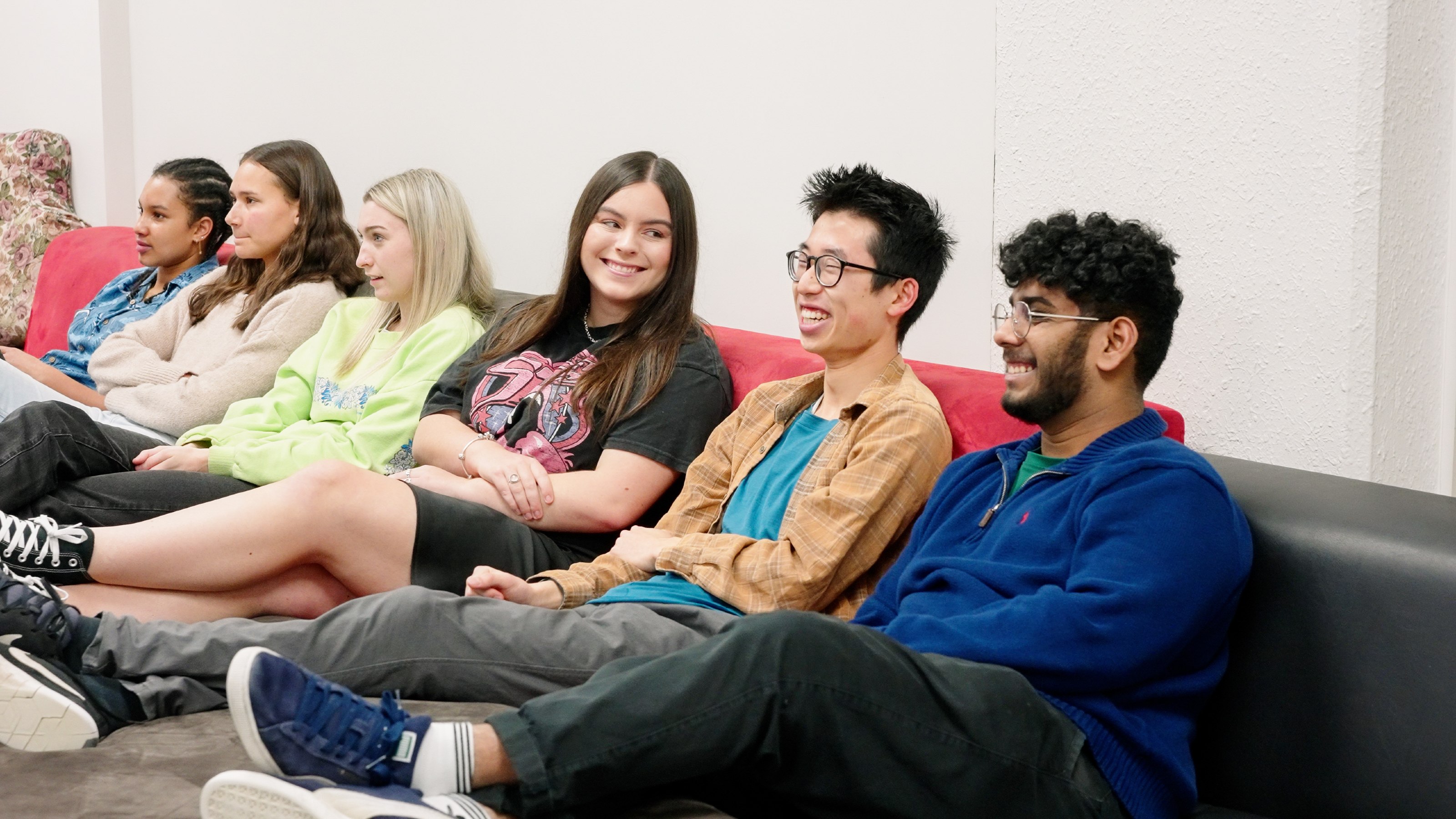 Six students sitting on couches, watching movie in hall common room.