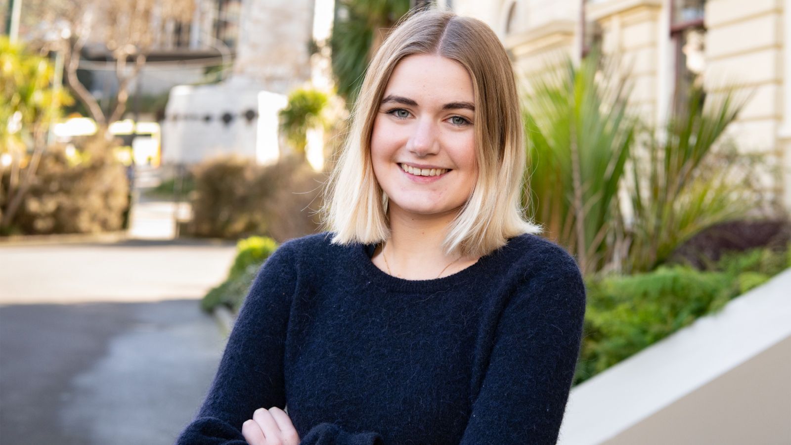 Girl with shoulder-length blond hair smiling at camera, green garden background